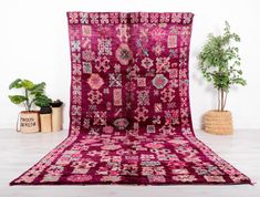 a large red rug with an intricate design on the front and back, sitting next to a potted plant