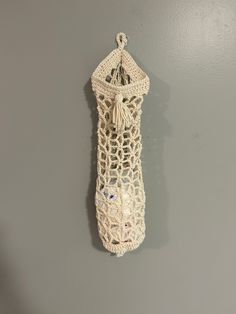 a white crochet bag hanging on the wall with a tasseled handle