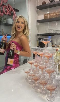 a woman in a pink dress holding a bottle of wine and glasses filled with champagne