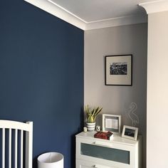 a white dresser sitting next to a blue wall in a room with pictures on it