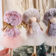 three handmade angel ornaments hanging from strings in front of a christmas tree and other decorations