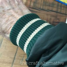 an old man wearing a green and white striped knitted arm warmer on his hand