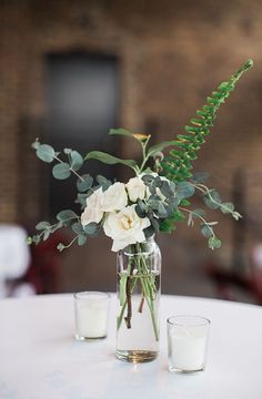 a vase filled with flowers and greenery sitting on top of a table next to two glasses