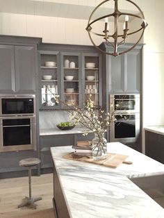 a kitchen with gray cabinets and marble counter tops, an island in the middle is surrounded by silver appliances