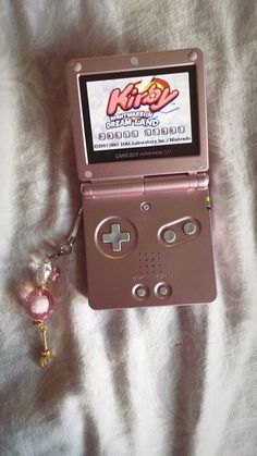 a pink nintendo gameboy with a keychain attached to it on a bed