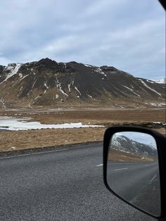 the side view mirror of a car driving on a road with snow covered mountains in the background