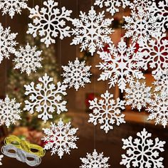 snowflakes and scissors hanging from strings in front of a christmas tree with lights