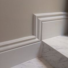 the corner of a bathroom with marble flooring and white trim on the shower wall