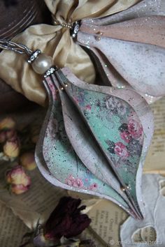 an ornament made out of paper and beads on a book with flowers in the background