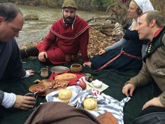 several people are sitting around a table with food on it and one person is wearing a red outfit