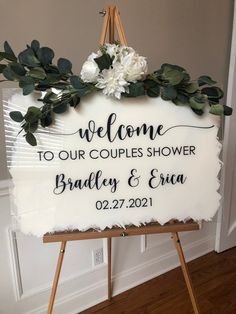 a welcome sign with greenery and flowers is displayed on a easel in front of a door