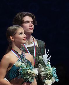 two people standing next to each other with flowers in their hands and medals around their necks