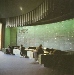 three people sitting at desks in an office with green tiles on the wall behind them