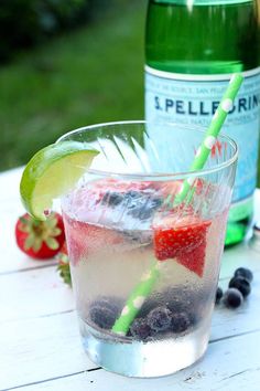 a glass filled with ice and berries next to a bottle of water on a table