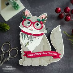 a christmas card with a cat wearing glasses and a ribbon around its neck, sitting next to some scissors