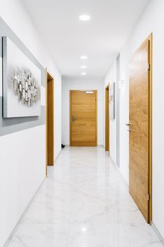 an empty hallway with two wooden doors and white marble flooring on either side of the room