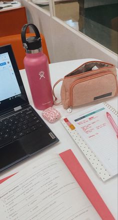 a laptop computer sitting on top of a white table next to a pink bag and notebook