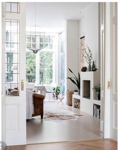 an open door leading to a living room with white walls and wooden floors, potted plants on the far wall