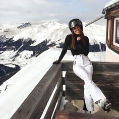 a woman sitting on top of a wooden bench next to snow covered mountains and skis