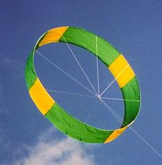 a large green and yellow kite flying in the blue sky with white clouds behind it