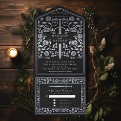 a black and white wedding stationery with greenery around it on a wooden table