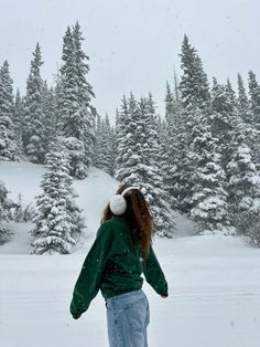 a woman standing in the snow with her back to the camera and trees behind her