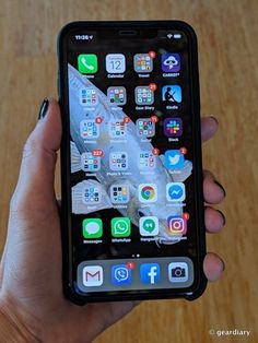 a person holding an iphone with icons on the screen and in their left hand, next to a wooden table