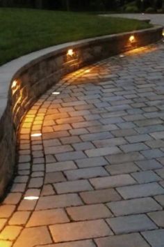 some lights that are on the side of a brick wall near a grass field and trees