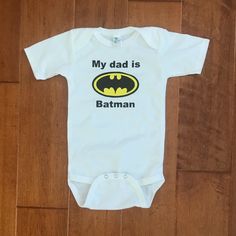 Never Worn, Never Washed Onesie With My Dad Is Batman On The Front! Originally Purchased From Bloomingdales Fitted Cartoon Print Onesie With Short Sleeves, Fitted Short Sleeve Onesie With Cartoon Print, Fitted Cartoon Print Short Sleeve Onesie, White Onesie With Character Print For Playtime, Fitted Onesie With Character Print For Playwear, Fitted Character Print Onesie For Playwear, Customizable Fitted Playful Onesie, Fitted Cartoon Print Onesie For Playwear, Cotton Onesie With Character Print