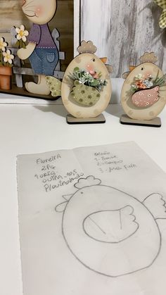 three figurines sitting on top of a table next to a drawing and flowers