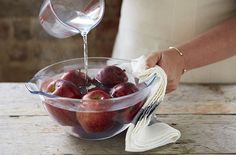 a person pouring water into a bowl filled with apples on top of a wooden table