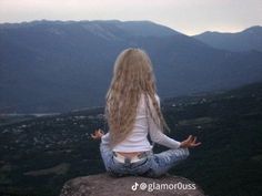 a woman sitting on top of a rock with her back to the camera and arms wide open