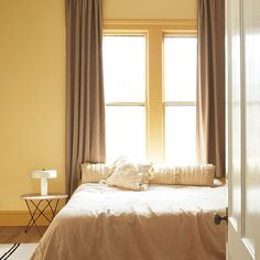 a bed sitting under a window next to a white door in a room with yellow walls