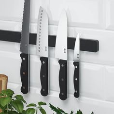 three knives are hanging on the wall next to a potted plant and knife holder