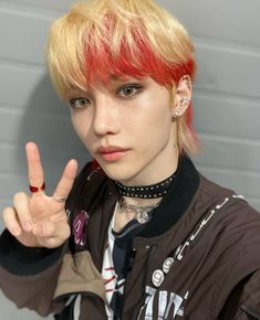 a person with red hair and piercings making the peace sign while wearing a jacket