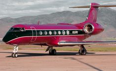 a red and black plane sitting on top of an airport tarmac with mountains in the background