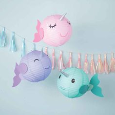 three paper fish hanging from a string with tassels attached to the line, one pink and one blue