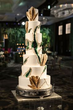 a three tiered white cake with gold leaf decorations on the top and bottom layer