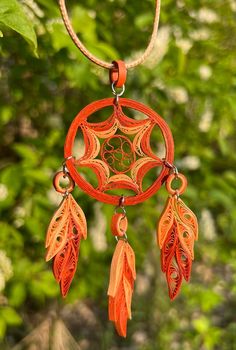 an orange dream catcher hanging from a tree branch with leaves on it's side