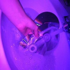 a person is washing their hands in a sink with purple lights on the wall behind them