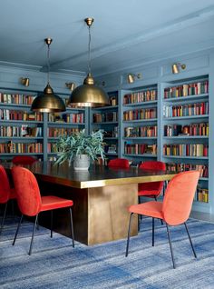 a dining room table with red chairs in front of bookshelves and blue carpet