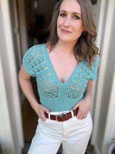 a woman standing in front of a door wearing white pants and a green top with crochet on it