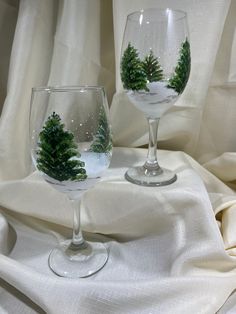 two wine glasses with christmas trees in them on a white cloth covered tableclothed surface