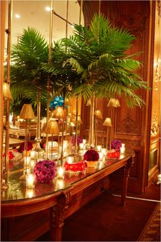 a table with flowers and candles on it in front of a large mirror that is reflecting the room