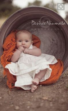 a baby is sitting in a bucket with an orange blanket on it's back