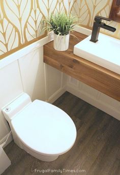 a white toilet sitting next to a wooden counter top under a bathroom mirror with a plant in it