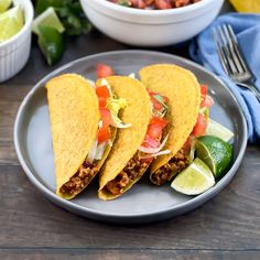 three tacos on a plate next to a bowl of salsa and lime wedges