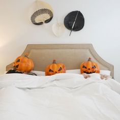 three carved pumpkins sitting on top of a bed in a room with white walls