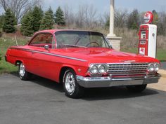 an old red car parked next to a gas pump