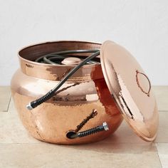 a large copper pot with two black wires in it and a lid on the ground